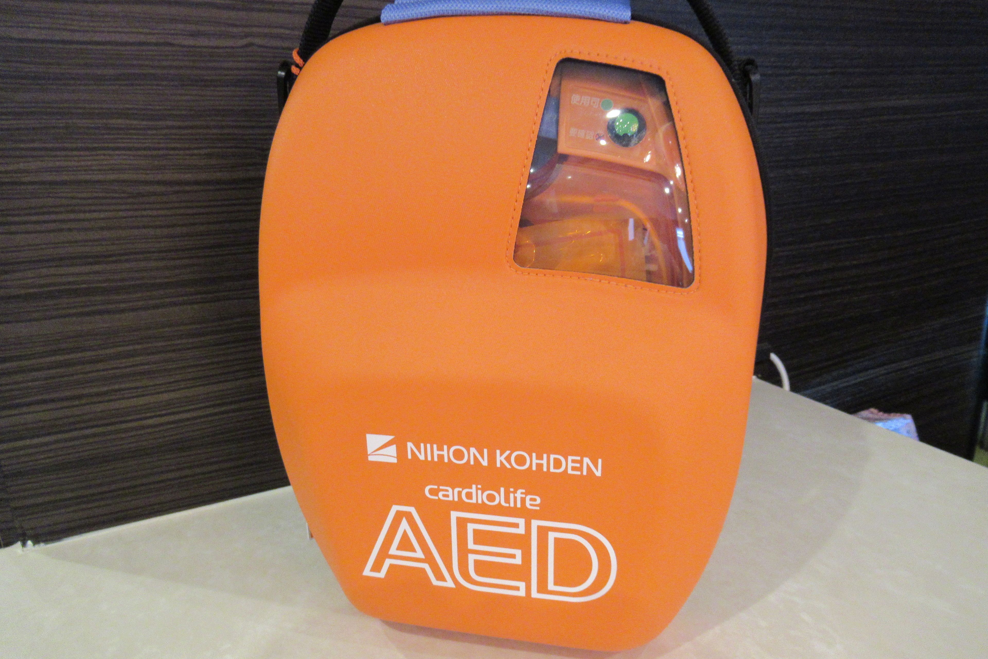 An orange AED (Automated External Defibrillator) bag with the text "NIHON KOHDEN cardiolife AED" on it.