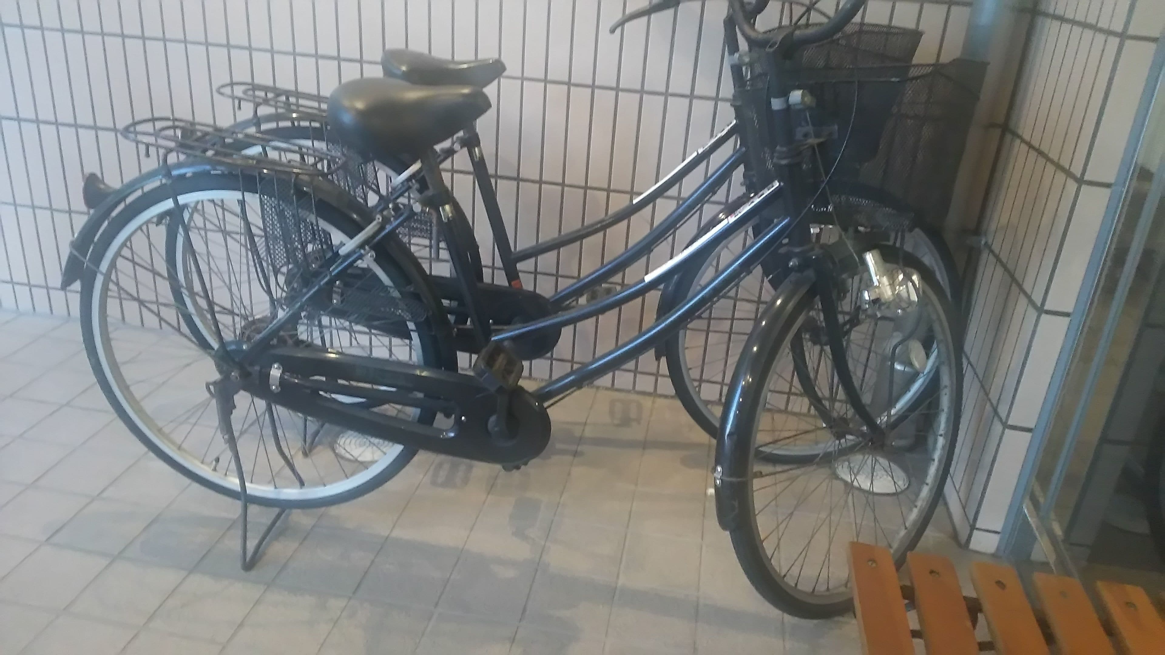 Sisällä, laatoitetussa tilassa, on parkkeerattu kuntopyörä, jossa on kori, ja taustalla on metallinen säleikköseinä.