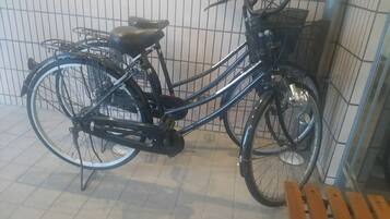 Un vélo d’appartement équipé d’un panier, placé à l’intérieur, sur un sol carrelé, avec un mur en treillis métallique.