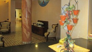 A lobby with a marble column, a reception desk, and a decorative plant arrangement. - Hotel Stazione sul lago di Iseo (Paratico)