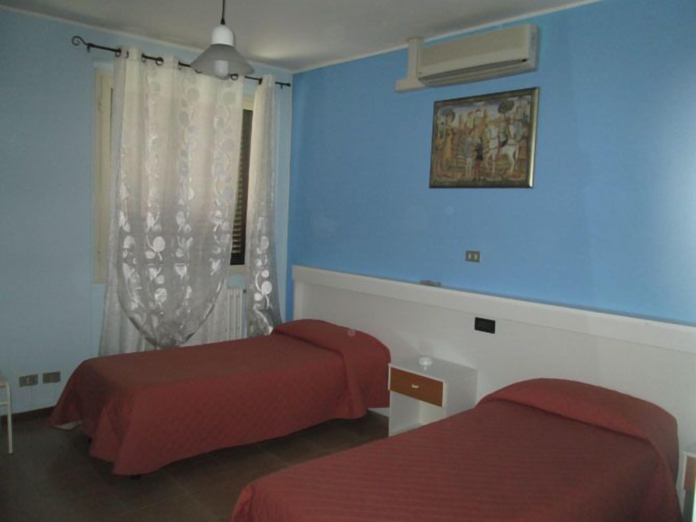 Une chambre avec deux lits, une fenêtre avec des rideaux, un ventilateur de plafond et un climatiseur fixé au mur.