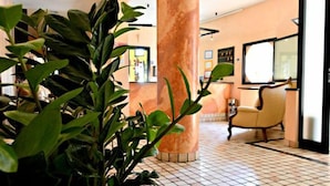 A lobby with a tiled floor, a large column, a reception desk, and a chair. - Hotel Stazione sul lago di Iseo (Paratico)