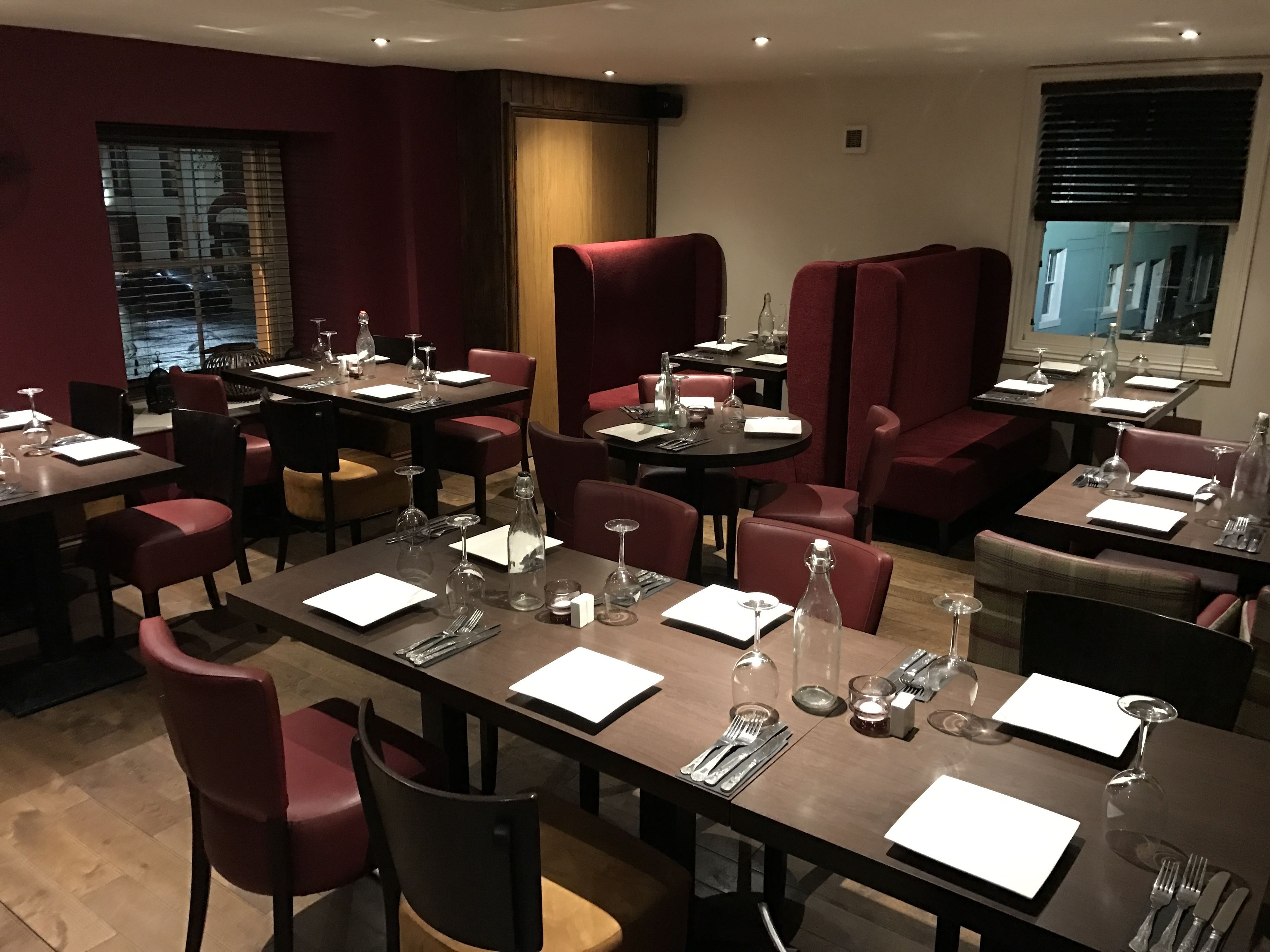 A restaurant with multiple tables and chairs, each set with cutlery and wine glasses.