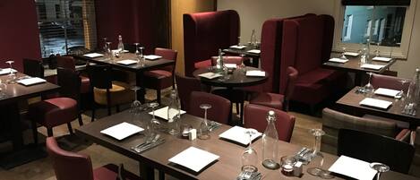 A restaurant with multiple tables and chairs, each set with cutlery and wine glasses.