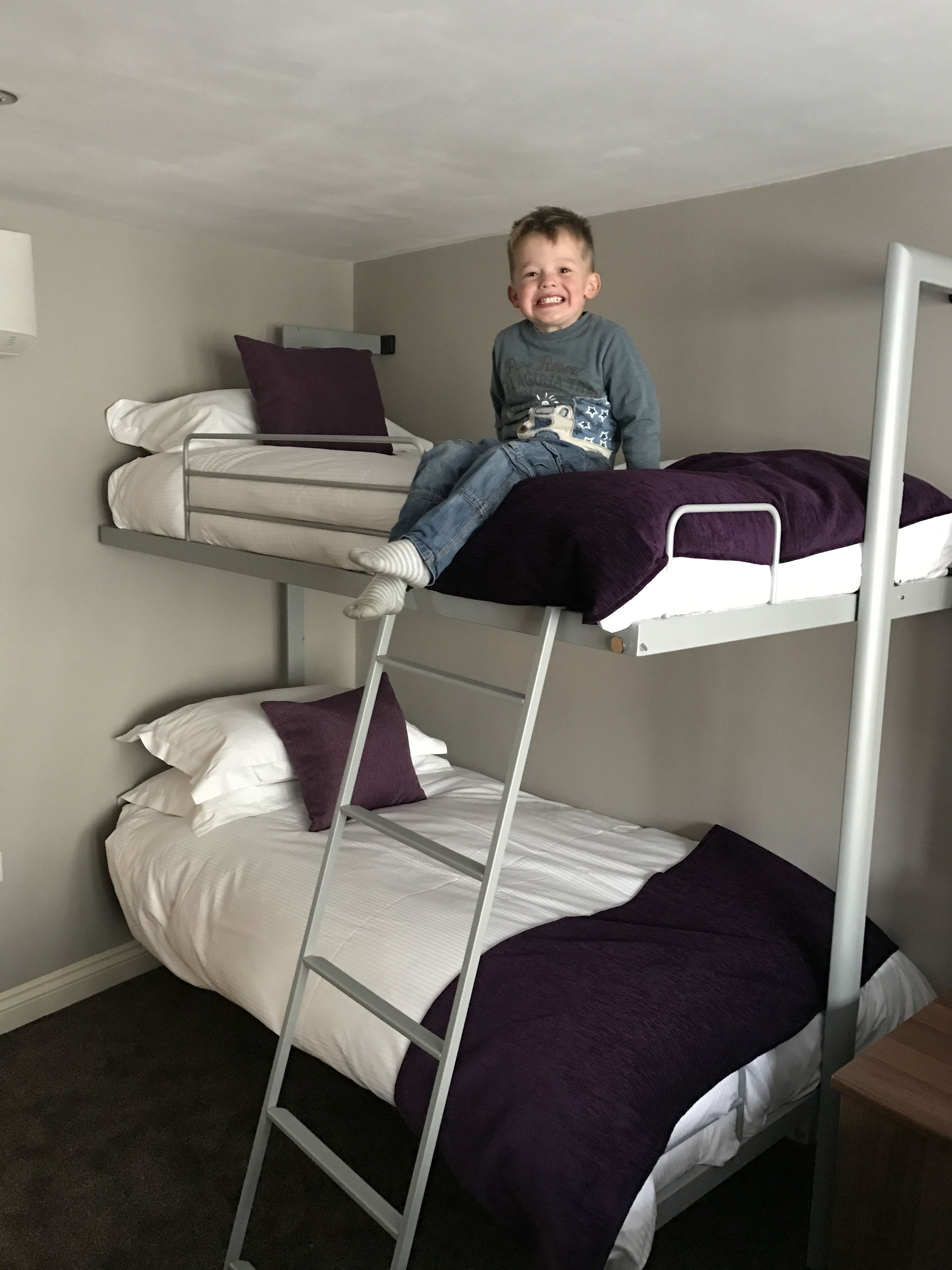 A bunk bed with two levels, each with white bedding and purple pillows.