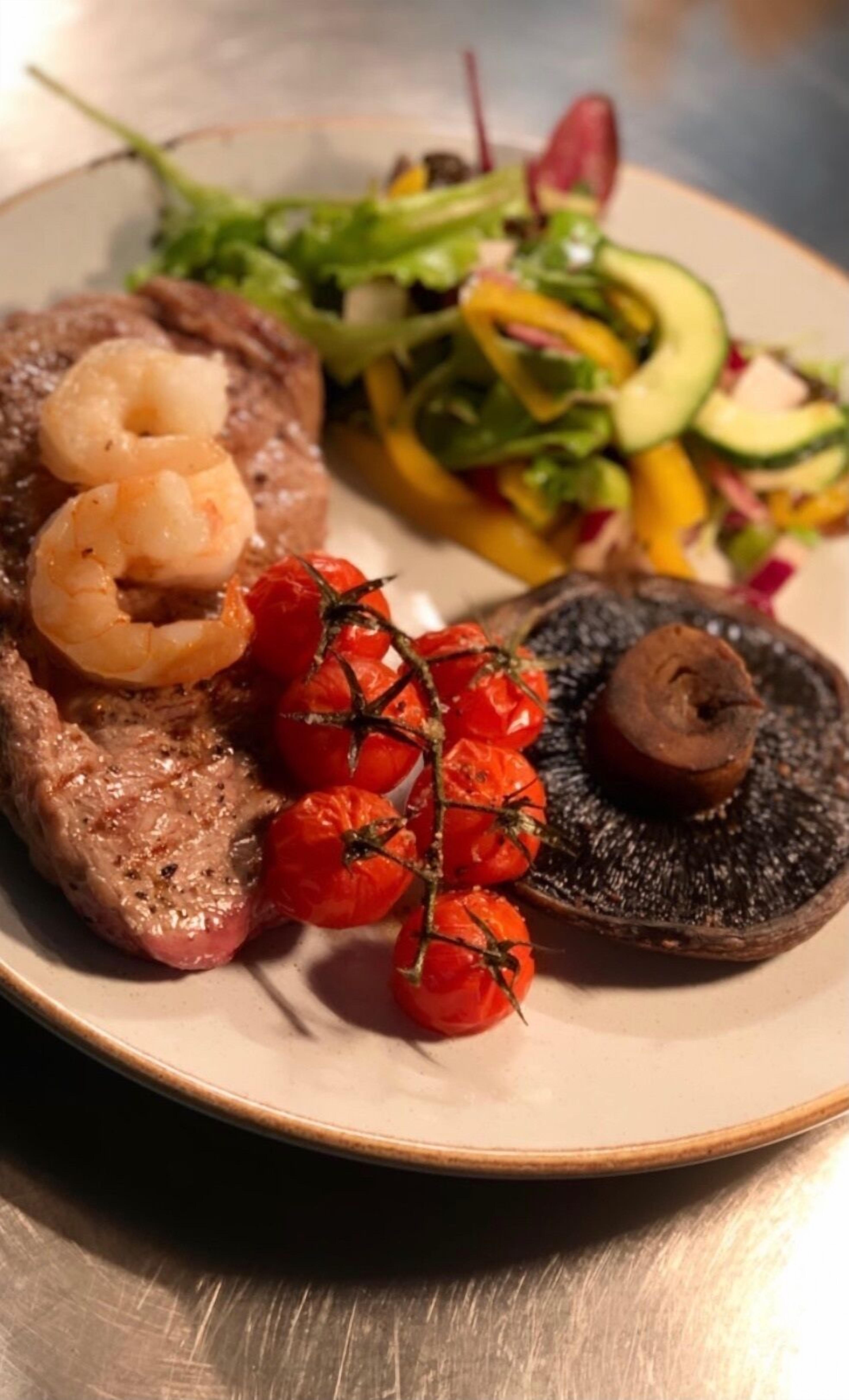 A plate with grilled steak, shrimp, cherry tomatoes, and a mushroom.