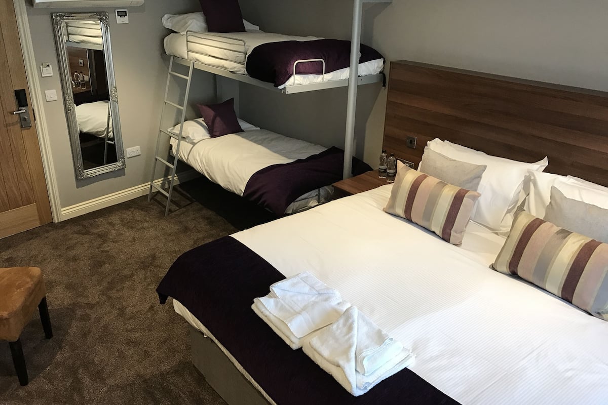 A hotel room with a bunk bed, a large mirror, a wooden headboard, and a carpeted floor.