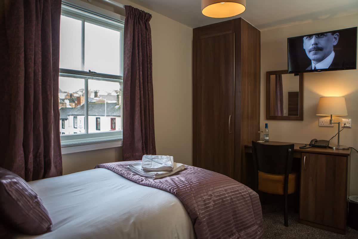 A hotel room with a bed, a desk, a chair, a television, and a window with curtains.