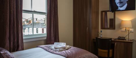 Una habitación de hotel con cama, escritorio, silla, televisión y ventana con cortinas.