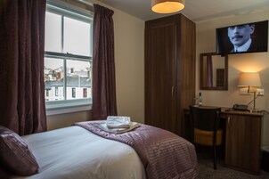 Una habitación de hotel con cama, escritorio, silla, televisión y ventana con cortinas.