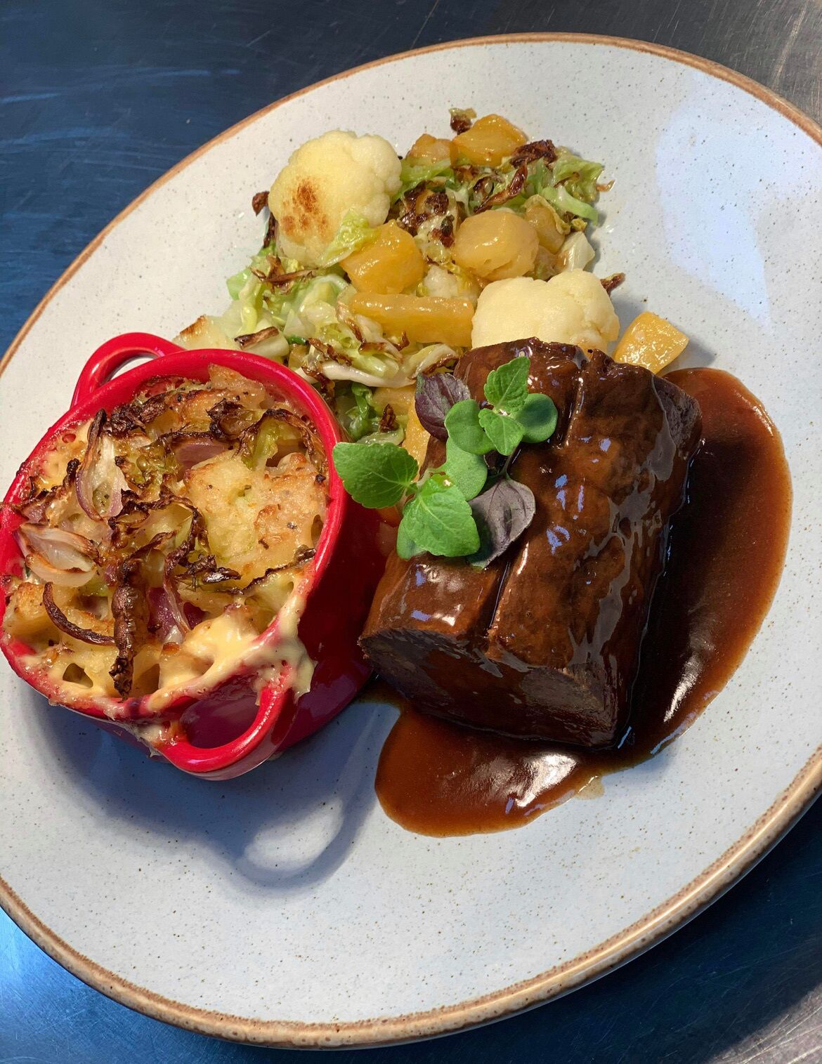 A plate with a stuffed red bell pepper, a piece of meat with gravy, and a side of potatoes and greens.