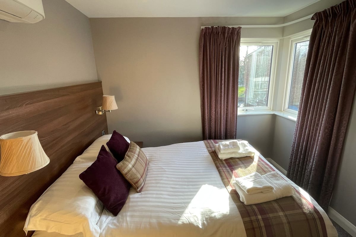 A hotel room with a large bed, a headboard, a bedside lamp, a window with curtains, and a view of the outside.