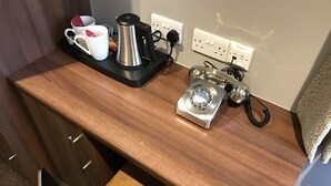 Un plan de travail en bois avec une machine à café, un téléphone et une prise électrique.