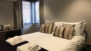 Une chambre d’hôtel avec un grand lit, un bureau avec un téléphone et une fenêtre avec des rideaux.