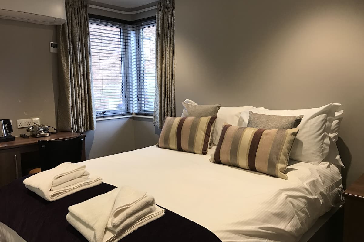 A hotel room with a large bed, a desk with a telephone, and a window with curtains.