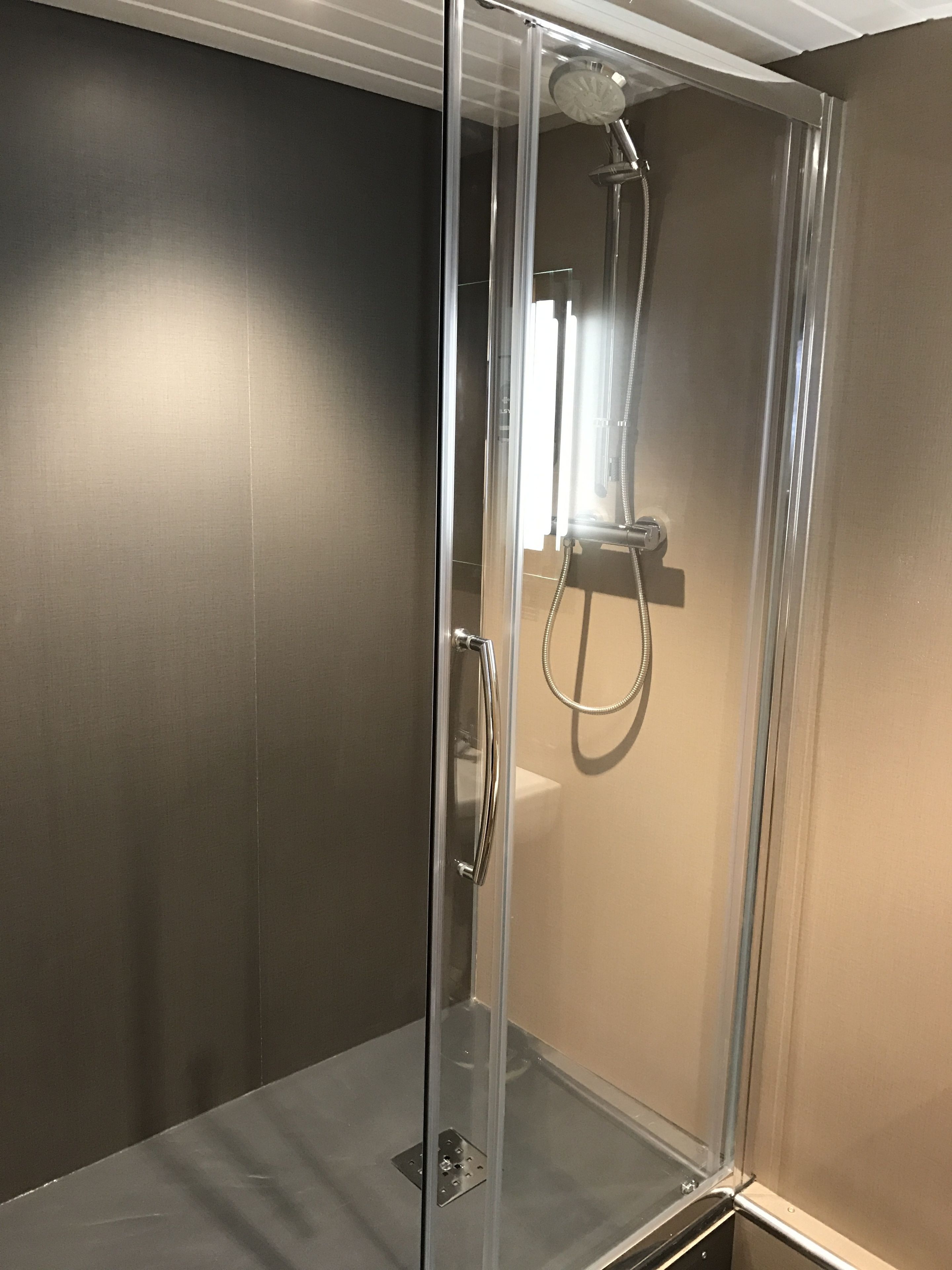 A glass-enclosed shower stall with a handheld showerhead and a wall-mounted faucet.