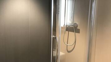 A glass-enclosed shower stall with a handheld showerhead and a wall-mounted faucet.