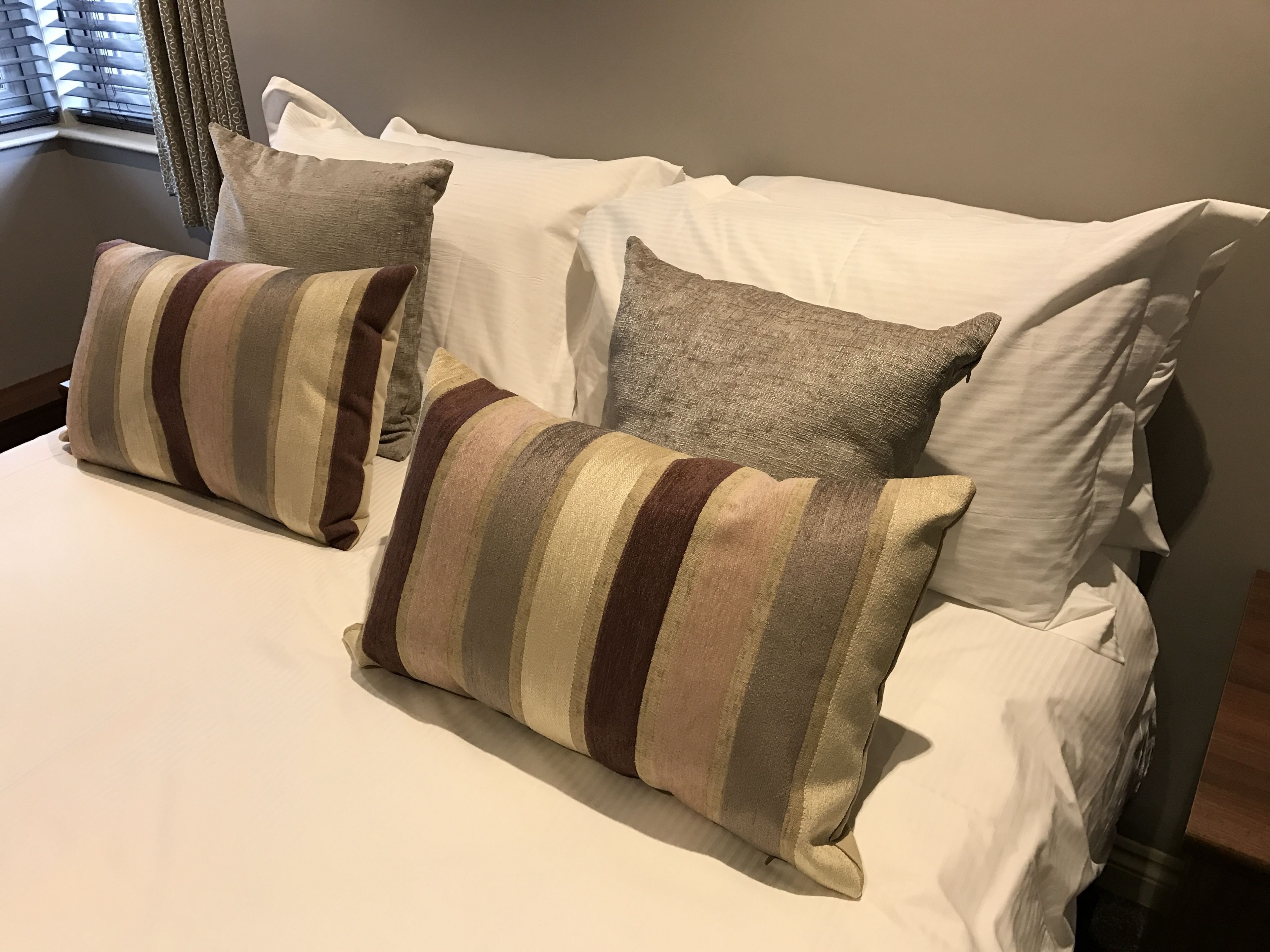 A bed with white linens and striped pillows.