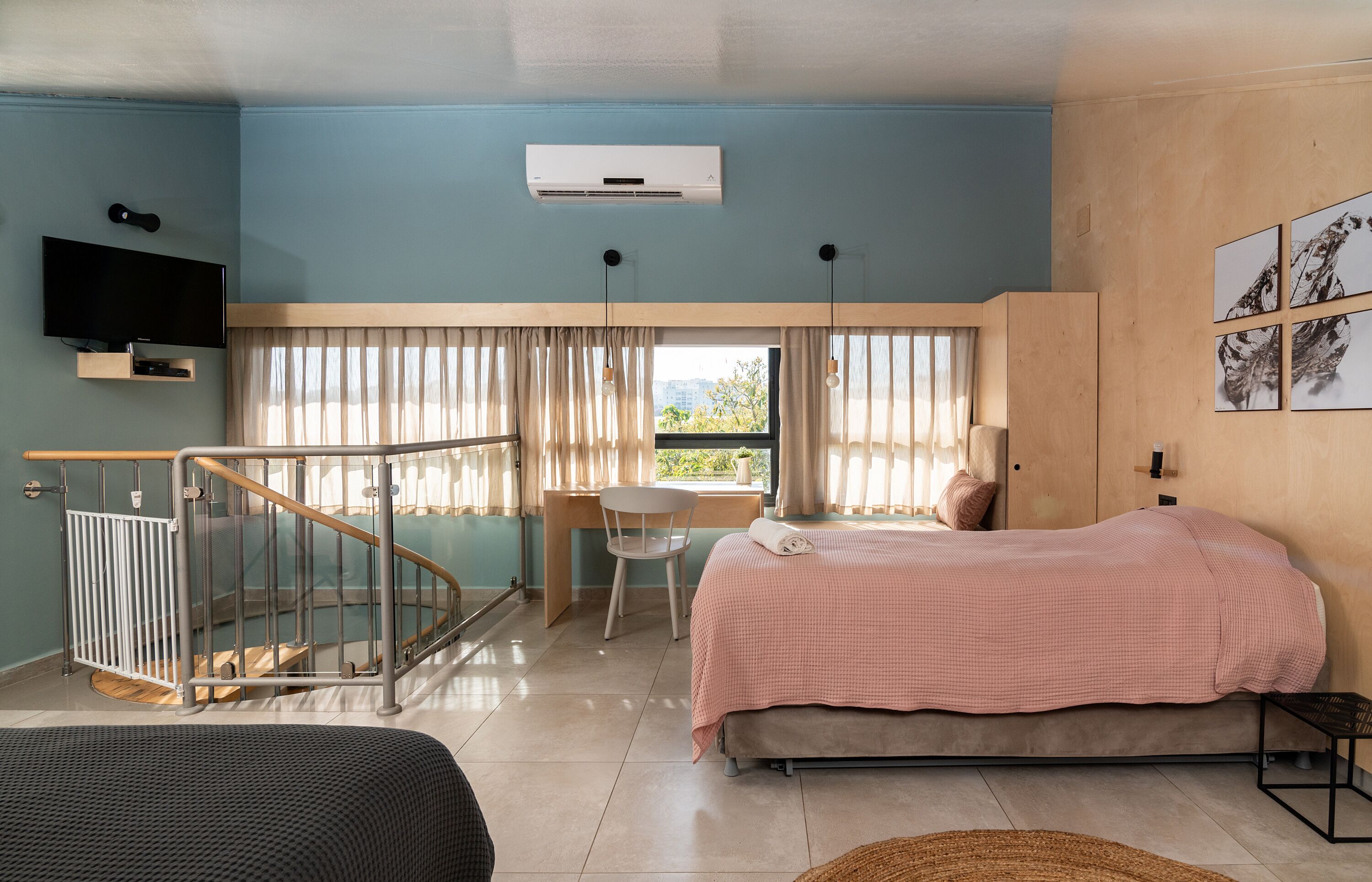 Ein Schlafzimmer mit Bett, Schreibtisch, Stuhl, Fernseher und Balkon.