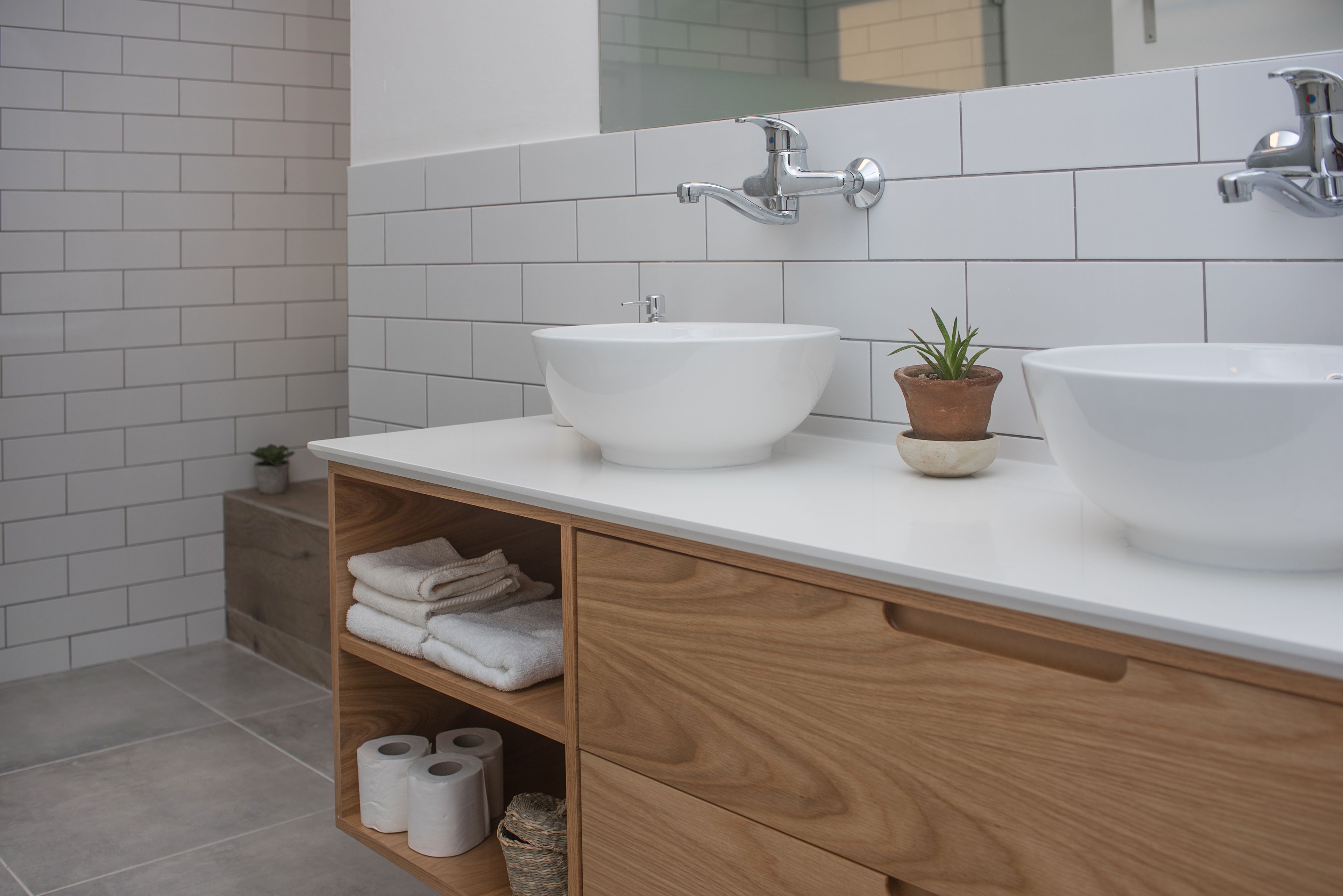Ein Badezimmer mit zwei weißen Waschbecken, einem Holz-Waschtisch, einem Spiegel und einer kleinen Topfpflanze.