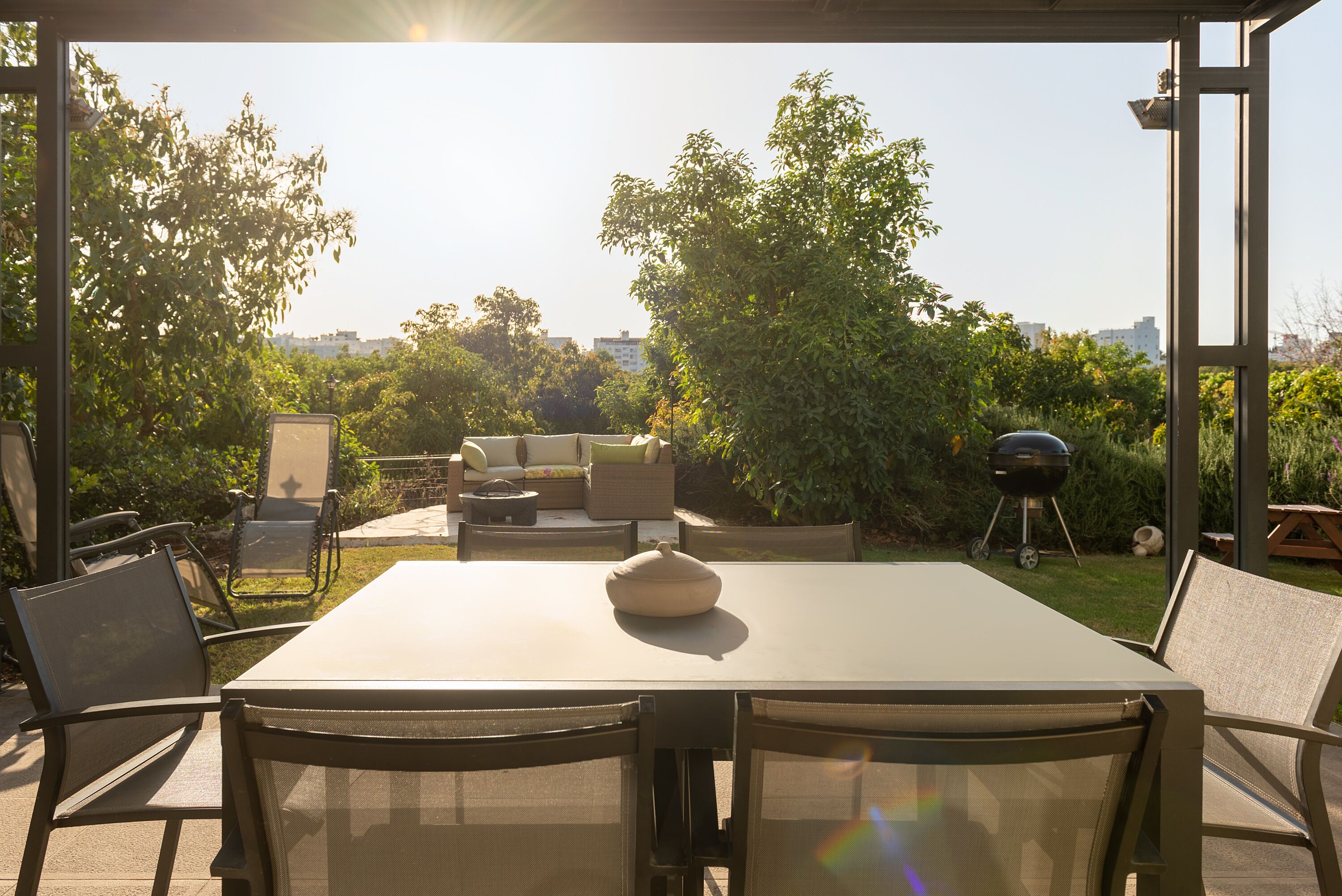 Um pátio externo com mesa e cadeiras, um conjunto de sofás e uma churrasqueira.