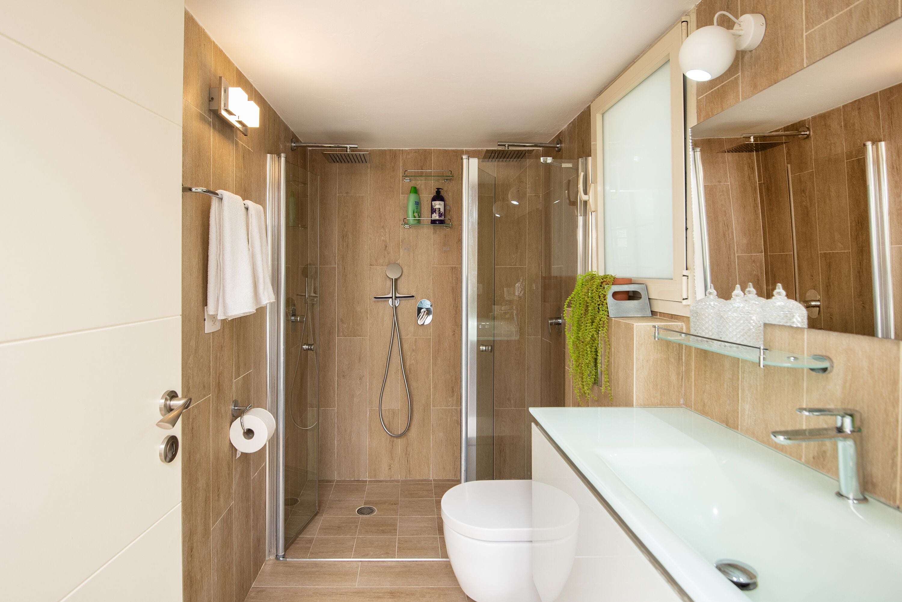 Une salle de bain moderne avec une douche à parois de verre, des toilettes blanches et un grand miroir au-dessus du lavabo.
