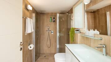 Une salle de bain moderne avec une douche à parois de verre, des toilettes blanches et un grand miroir au-dessus du lavabo.