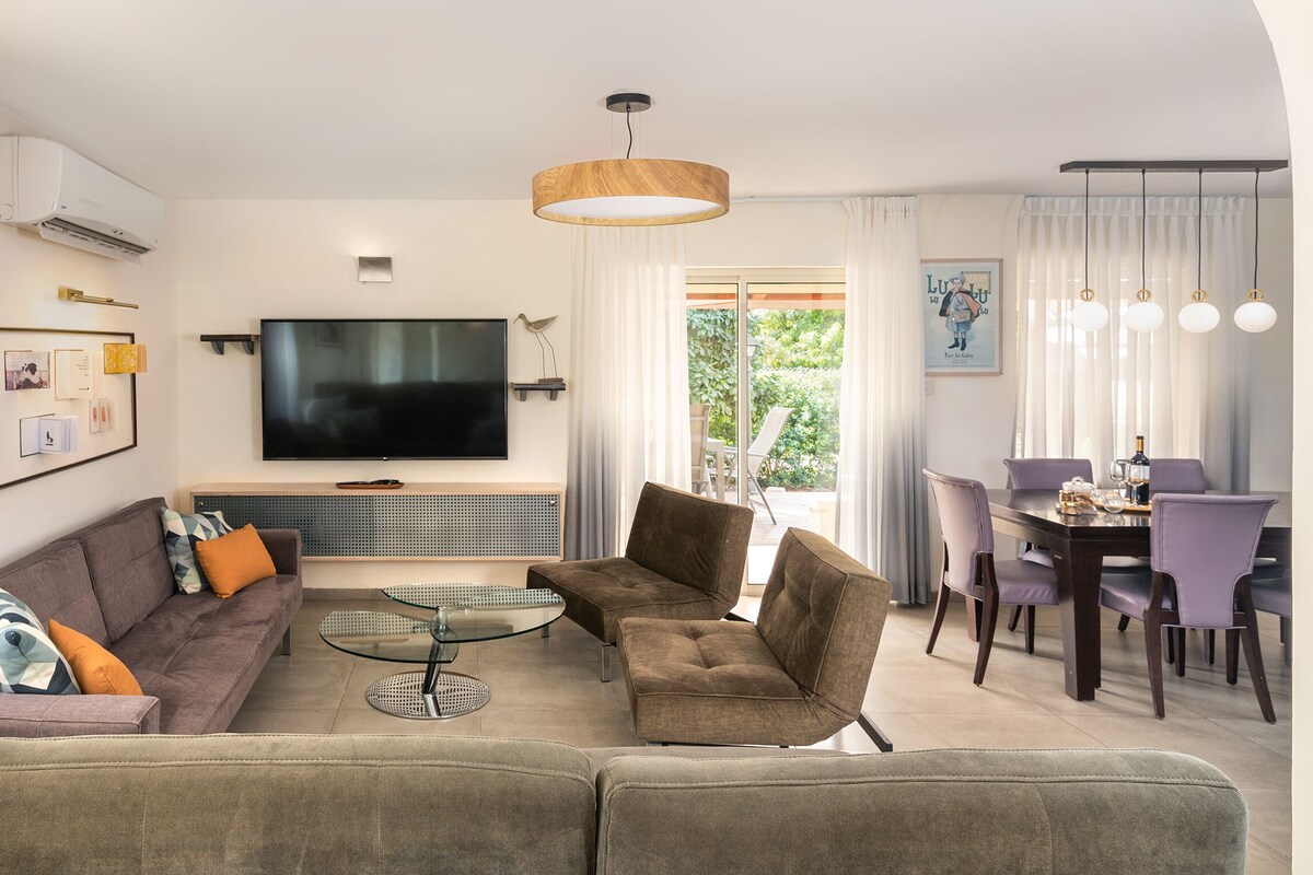 A modern living room with a sofa, armchairs, a coffee table, and a dining area with a table and chairs.
