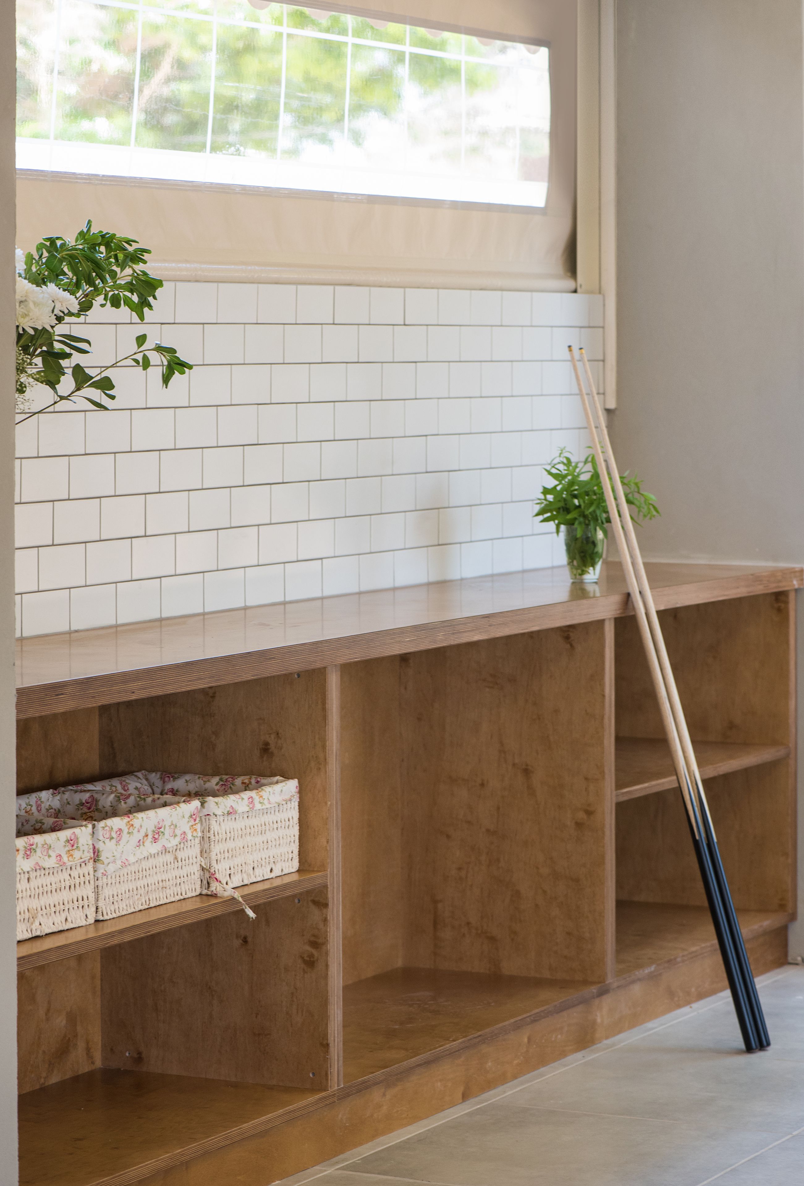 Una habitación con estante de madera, ventana con persianas y una planta.