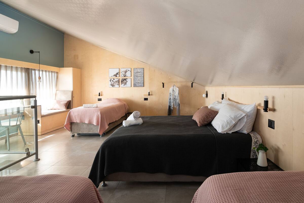 A bedroom with two beds, a desk, and a chair. There are wall-mounted lights and a window with curtains.