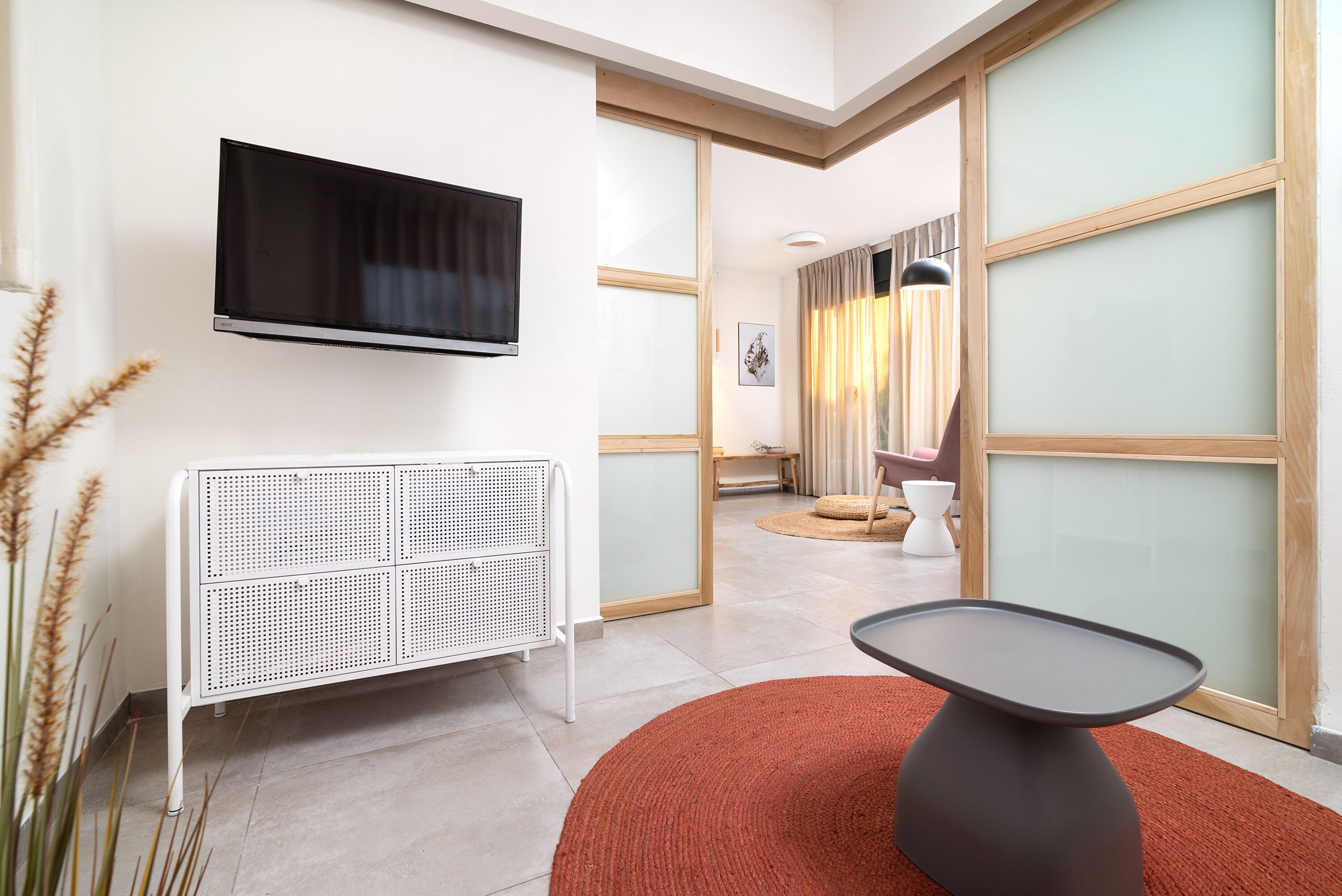 Habitación de hotel moderna con televisor de pantalla plana, radiador blanco, alfombra roja y vista de la habitación contigua.