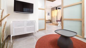 Habitación de hotel moderna con televisor de pantalla plana, radiador blanco, alfombra roja y vista de la habitación contigua.