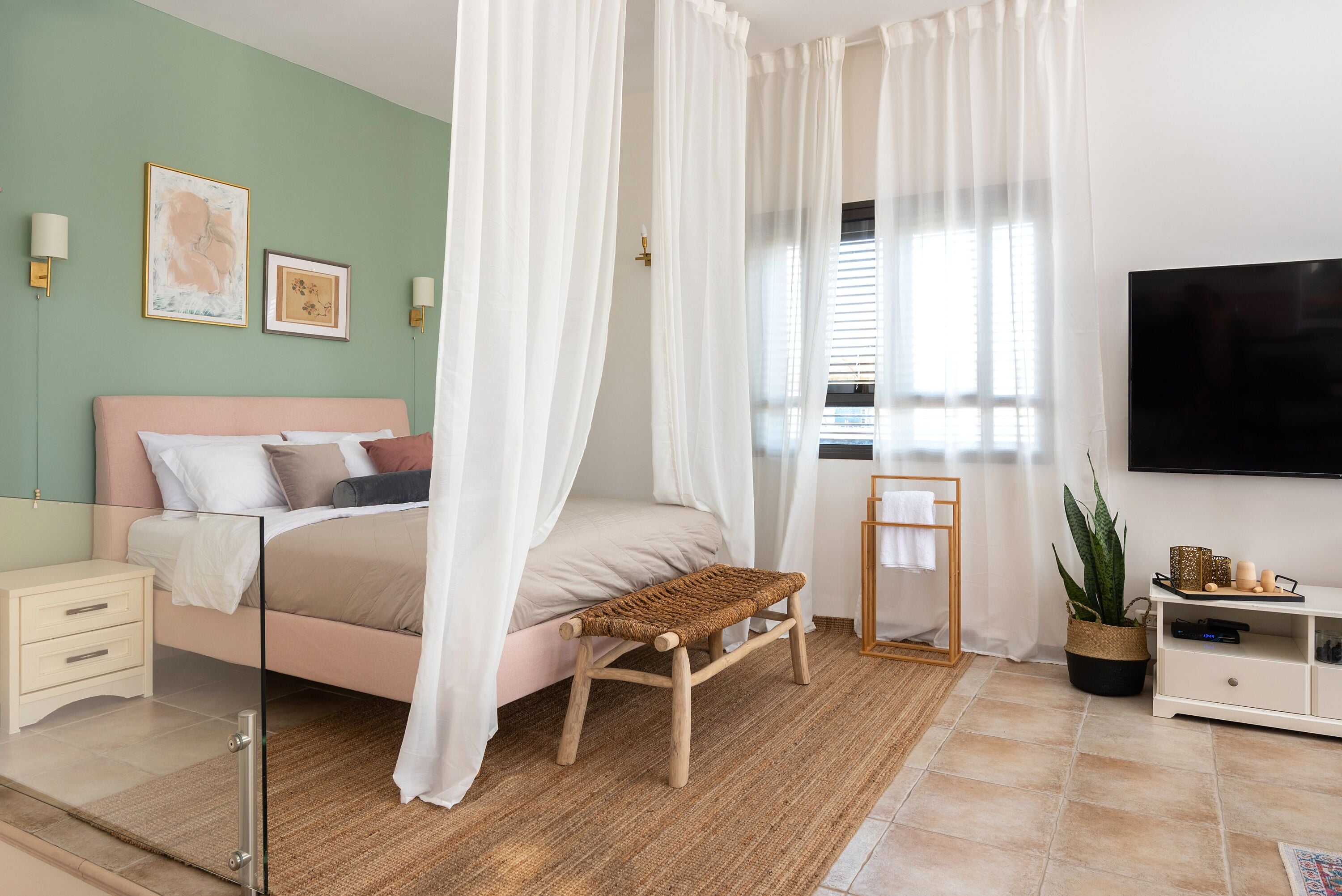 Un dormitorio con cama, mesita de noche, televisor y ventana con cortinas.