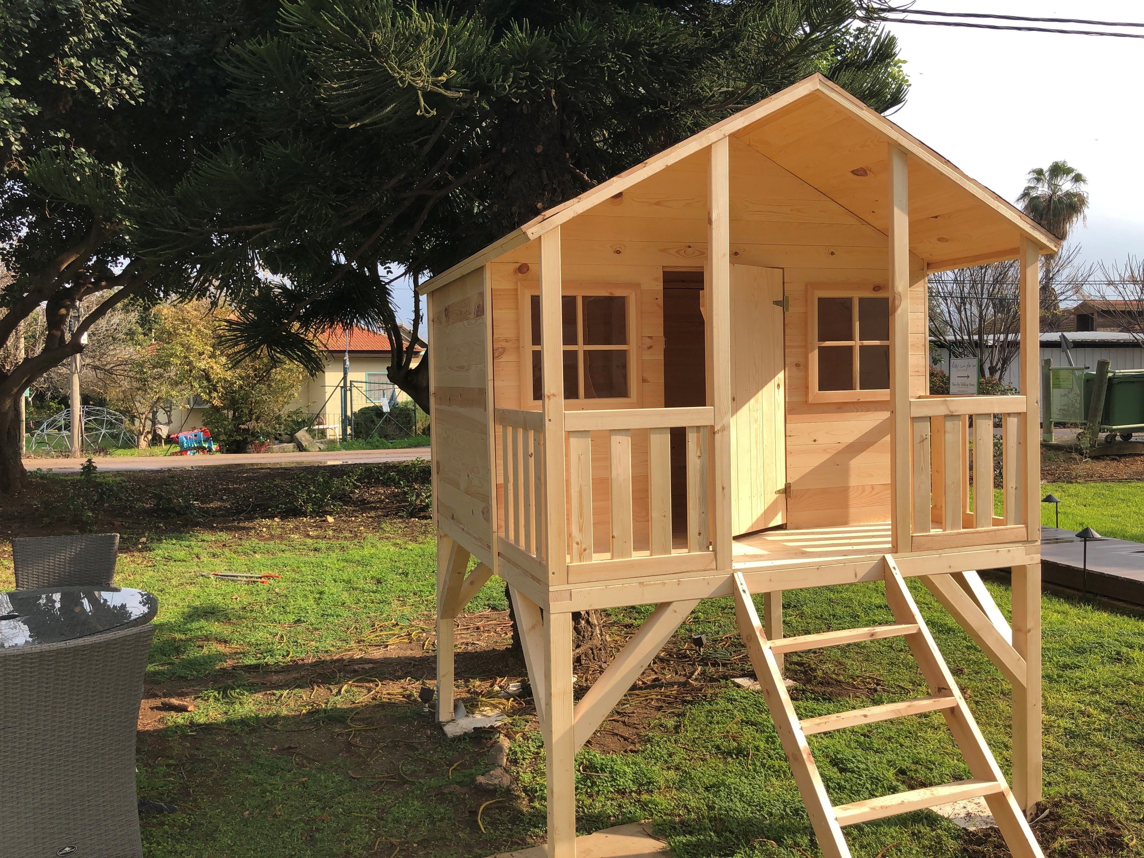 A wooden playhouse with a ladder, a small door, and windows.