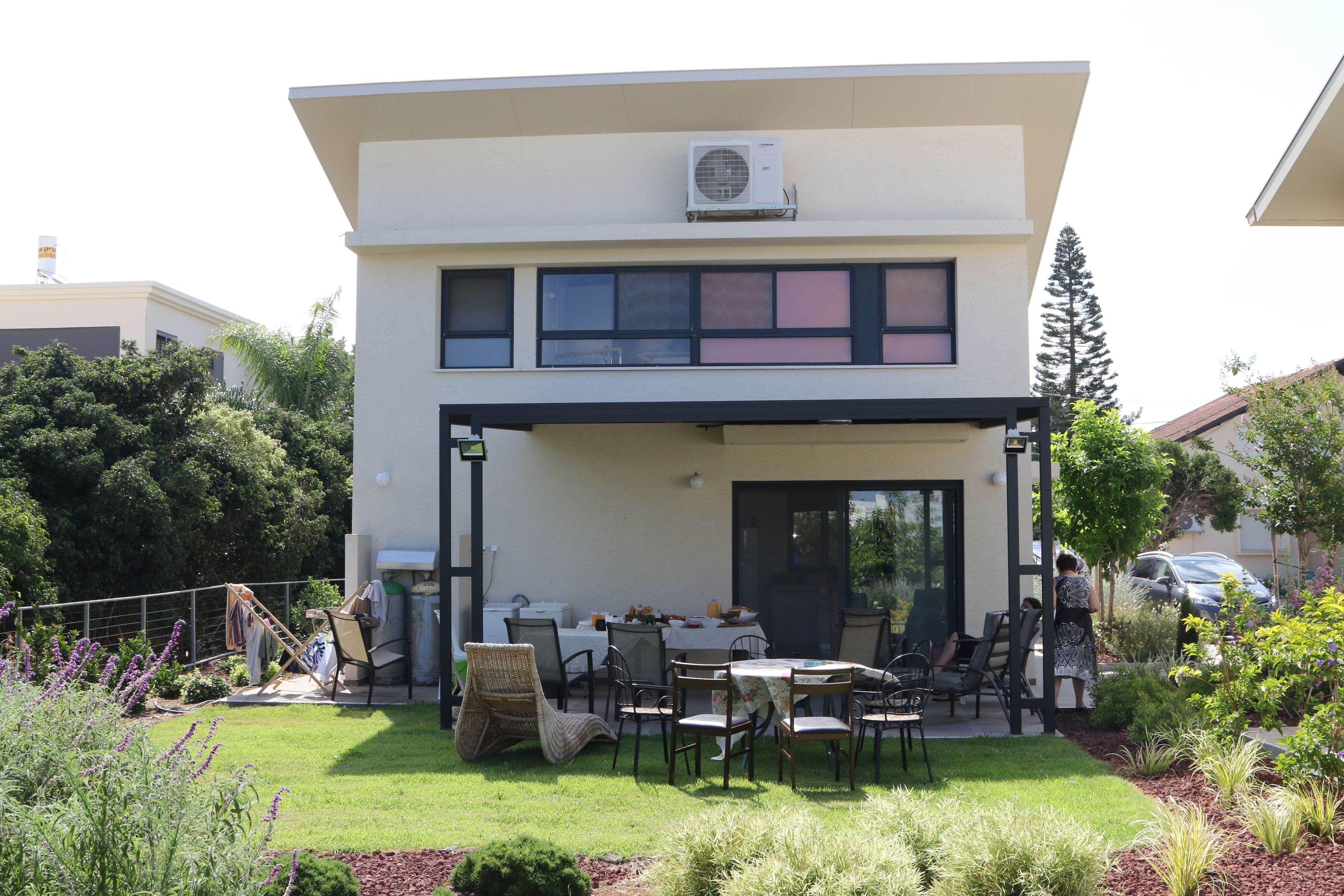 A modern two-story house with a covered patio area featuring outdoor seating and a dining table.