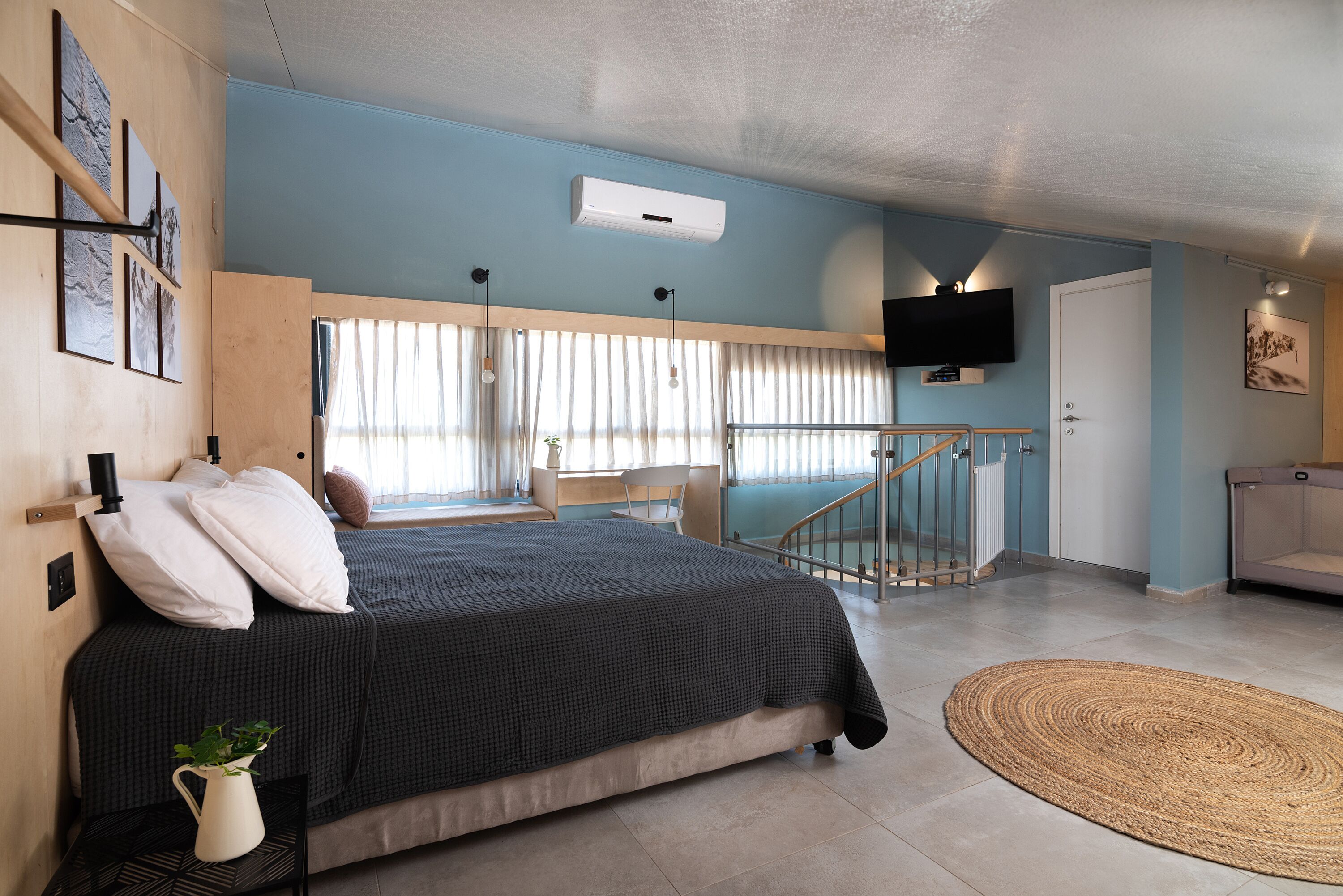 A bedroom with a bed, a TV, a staircase, and a view of the outside.