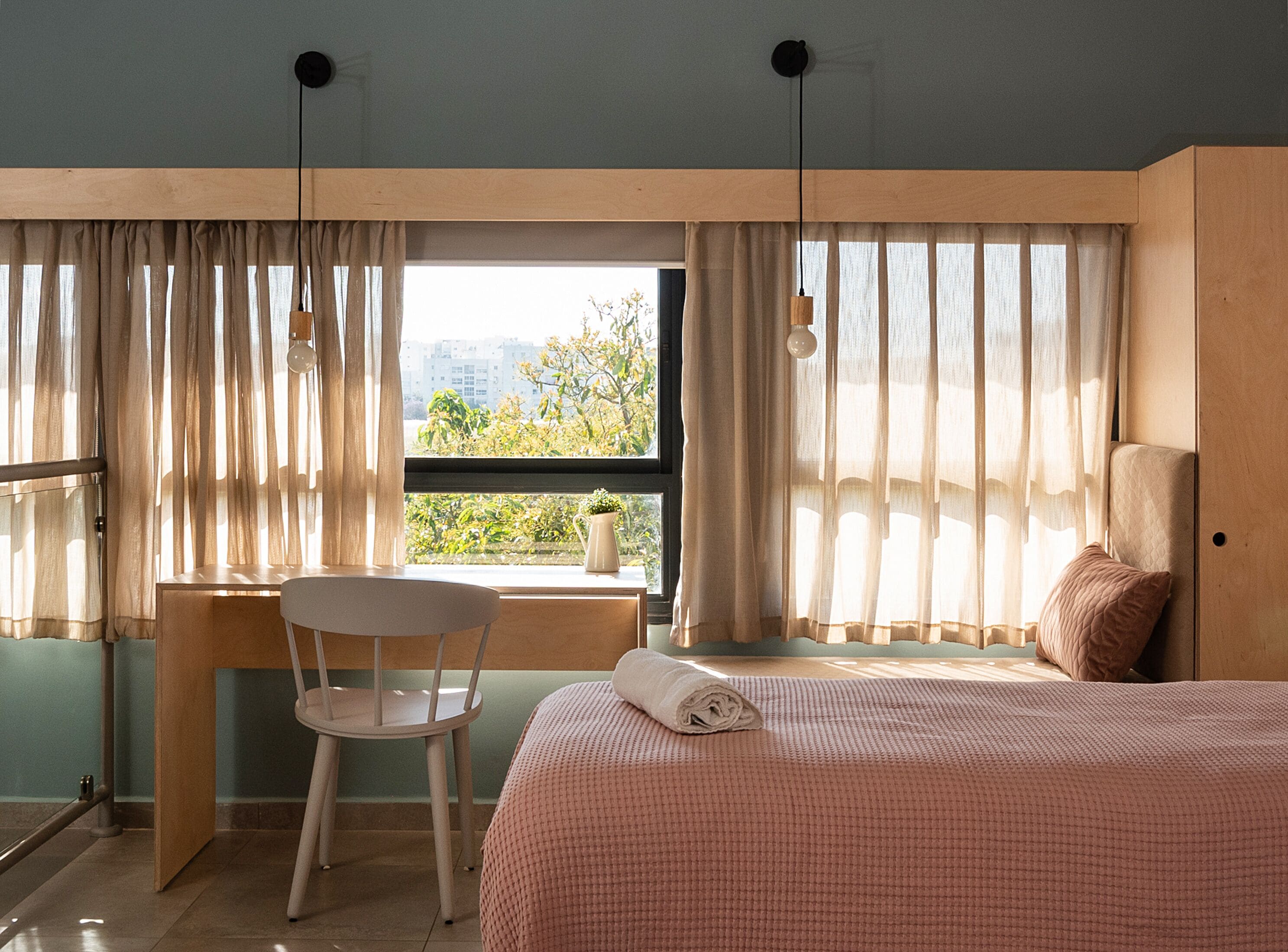 Un dormitorio con cama, una silla, un escritorio y una ventana con cortinas.