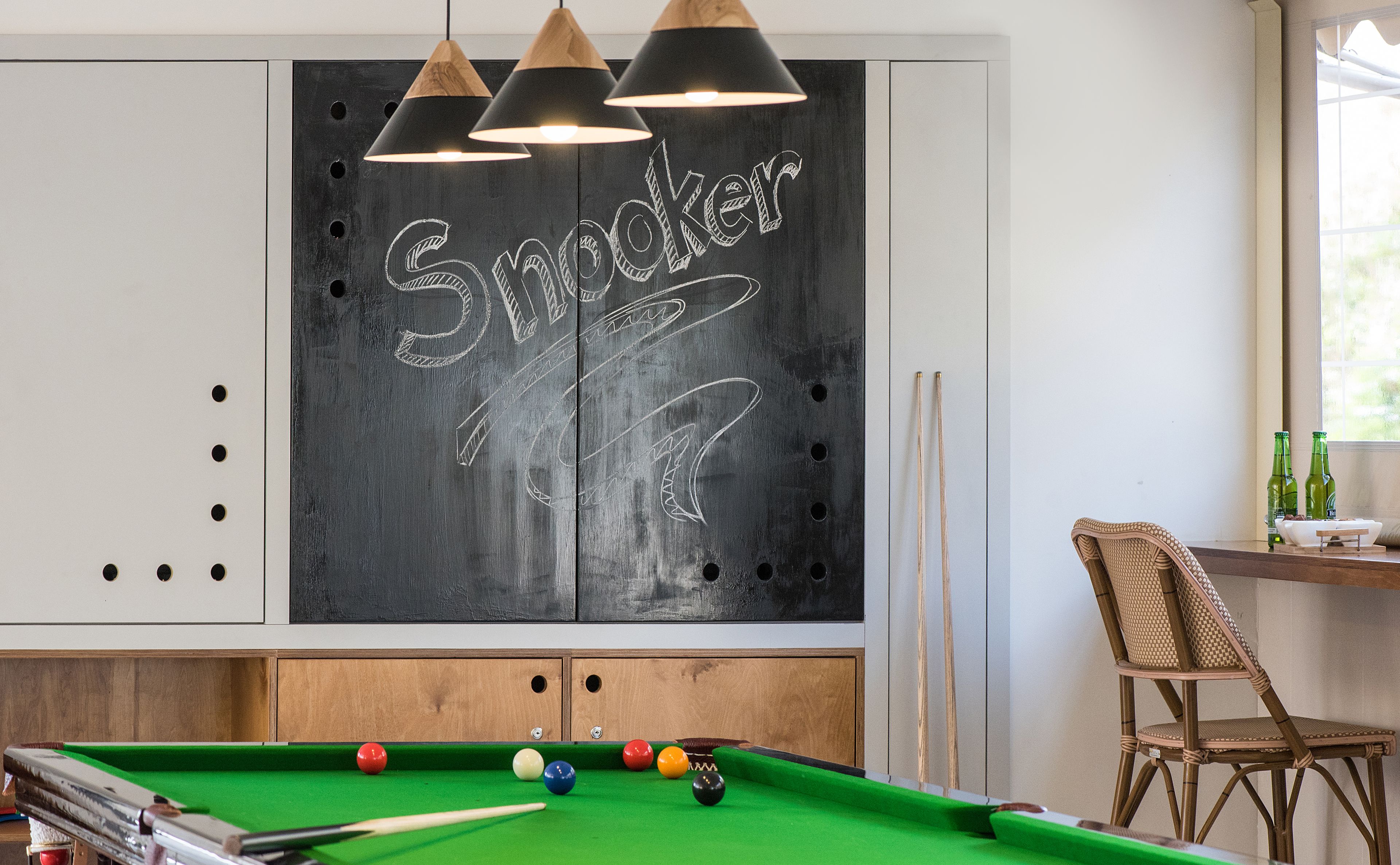 A billiards table with balls and cues, a chalkboard with 'Snooker' written on it, and a wicker chair.