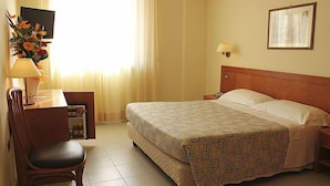 Habitación de hotel con cama, escritorio con lámpara, silla, televisor y un cuadro en la pared.
