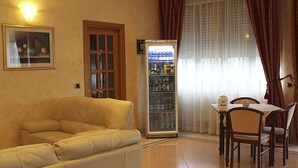 Una sala de estar con un sofá color beige, una mesa de comedor con sillas, un refrigerador y una ventana con cortinas.