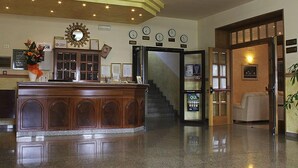 Zona de recepción con un mostrador de madera, un espejo grande, varios relojes y una escalera que sube a otro piso.