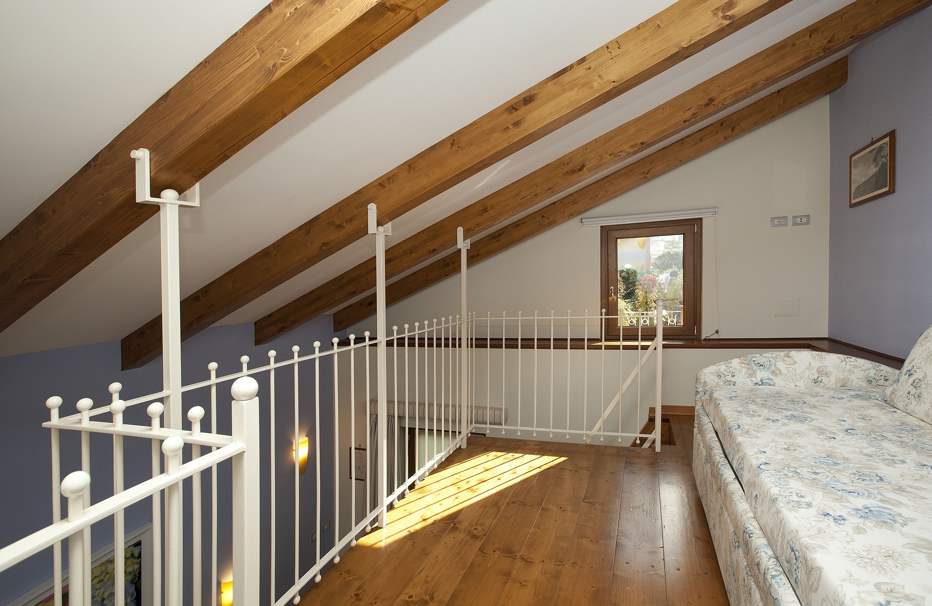 A bedroom with a wooden ceiling, a white bed, and a window with a view of greenery.