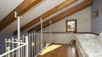 A bedroom with a wooden ceiling, a white bed, and a window with a view of greenery.