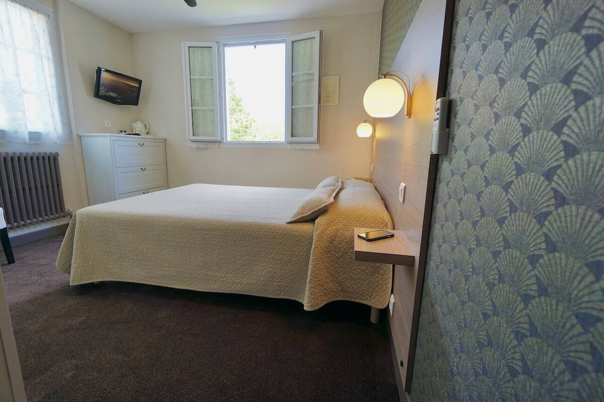 A bedroom with a bed, bedside table, lamp, and a TV on the wall.