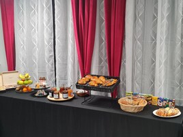 Une table de buffet proposant une variété d’aliments, notamment des fruits, des pâtisseries et des condiments.