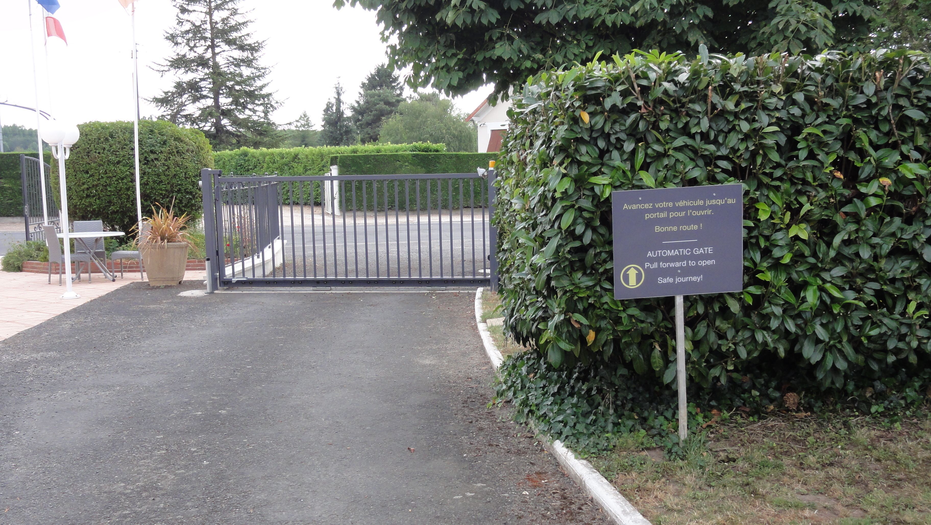 A gated entrance with a sign instructing to pull forward to open the automatic gate.