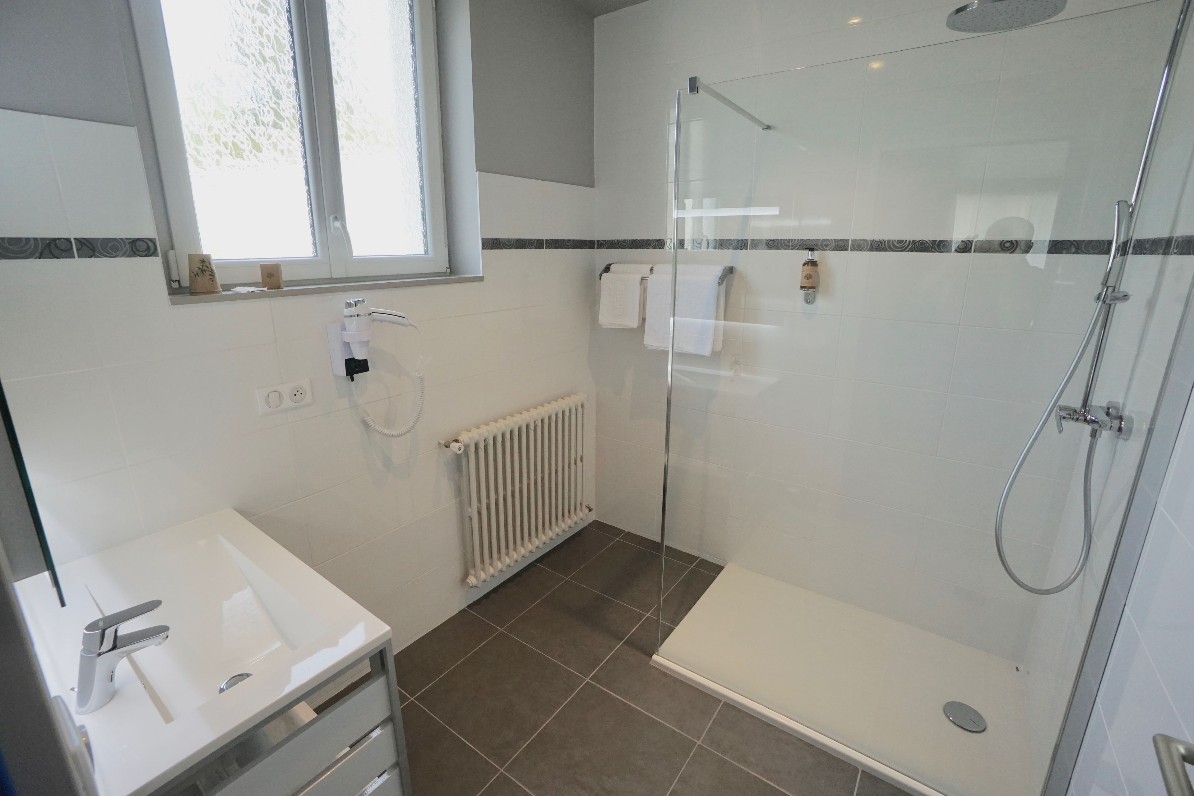 A modern bathroom with a glass-enclosed shower, a white sink, and a tiled floor.