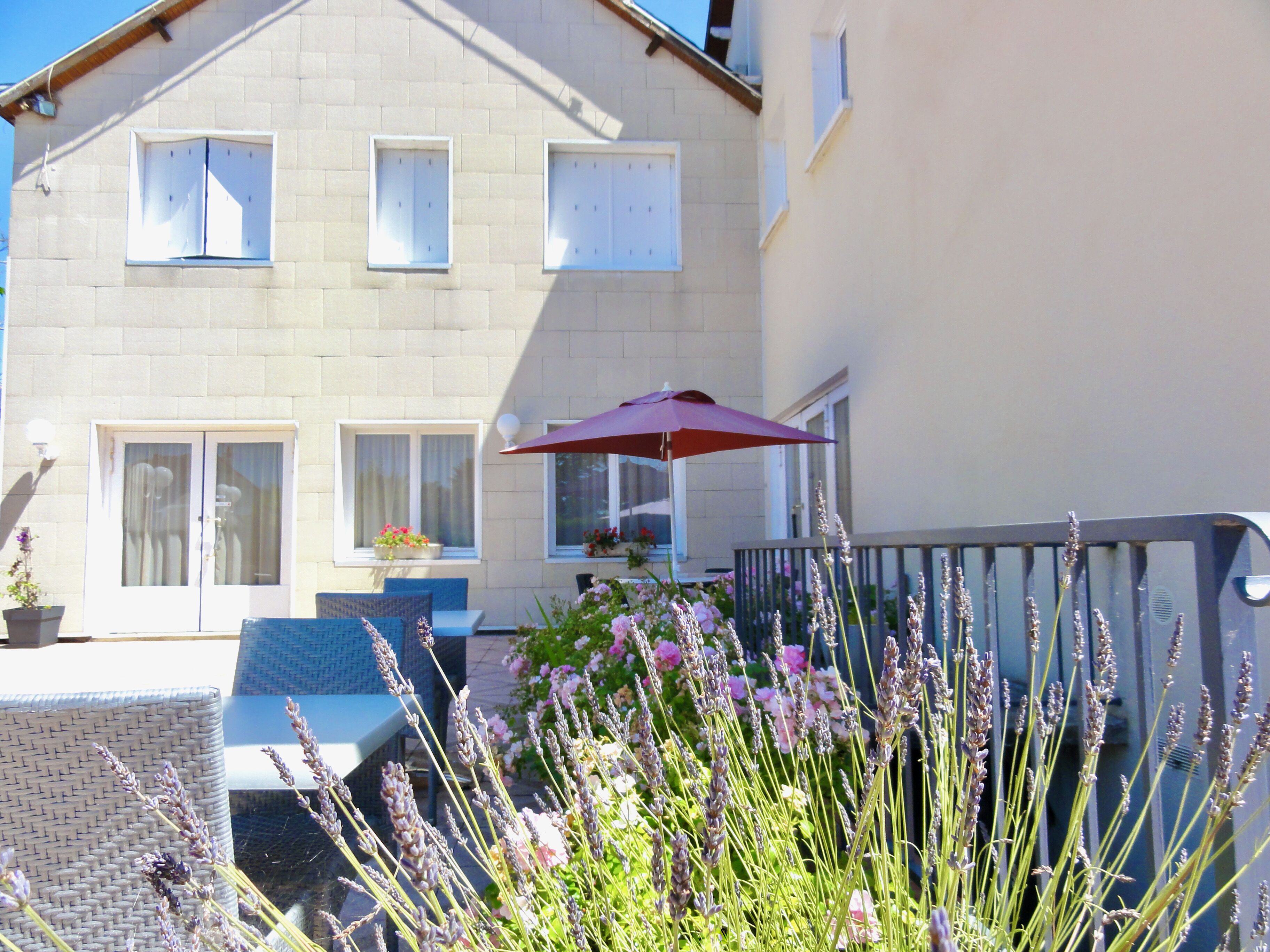 A two-story building with a balcony, outdoor seating, and potted plants.