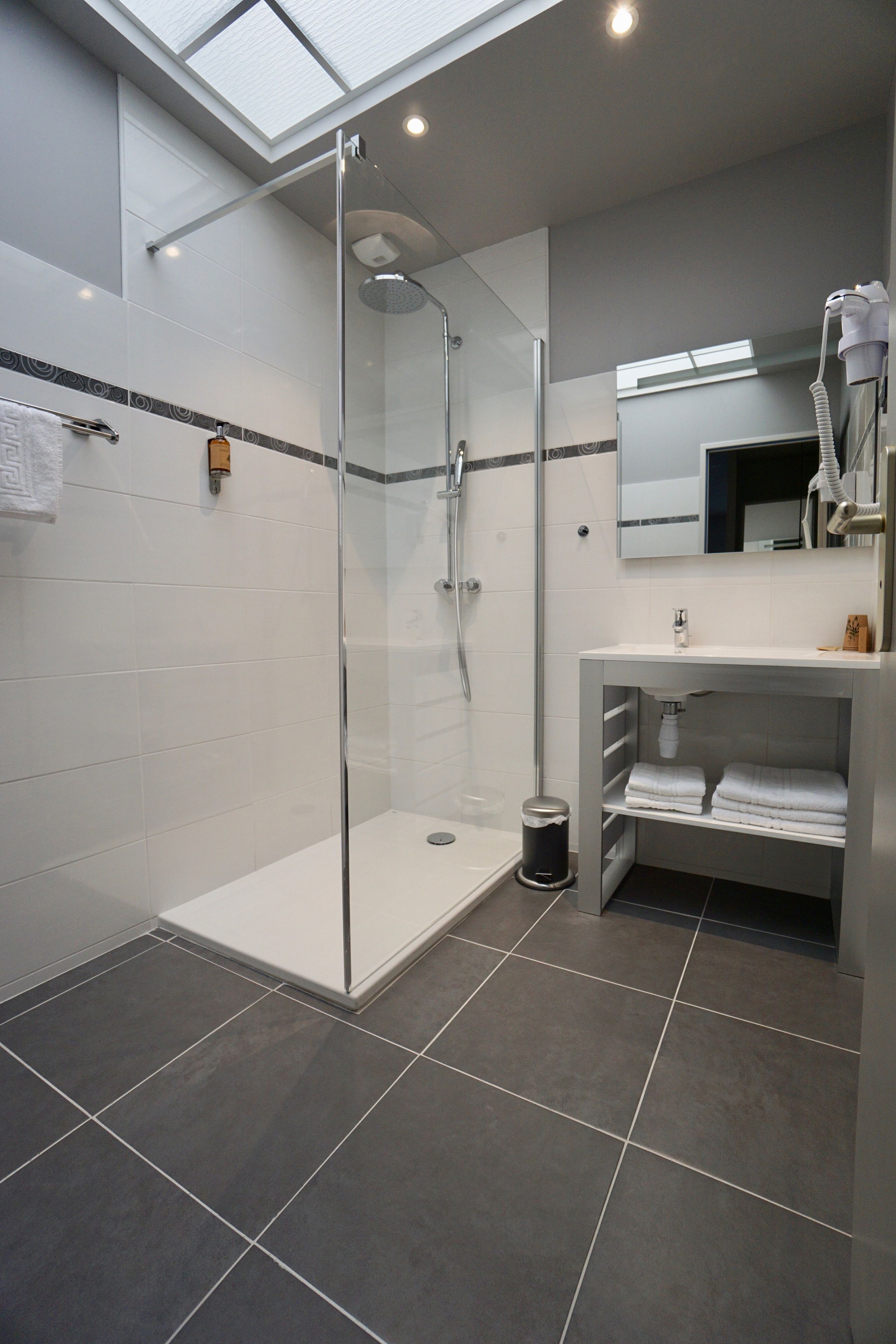 A modern bathroom with a glass-enclosed shower, white tiles, and a vanity with a mirror.
