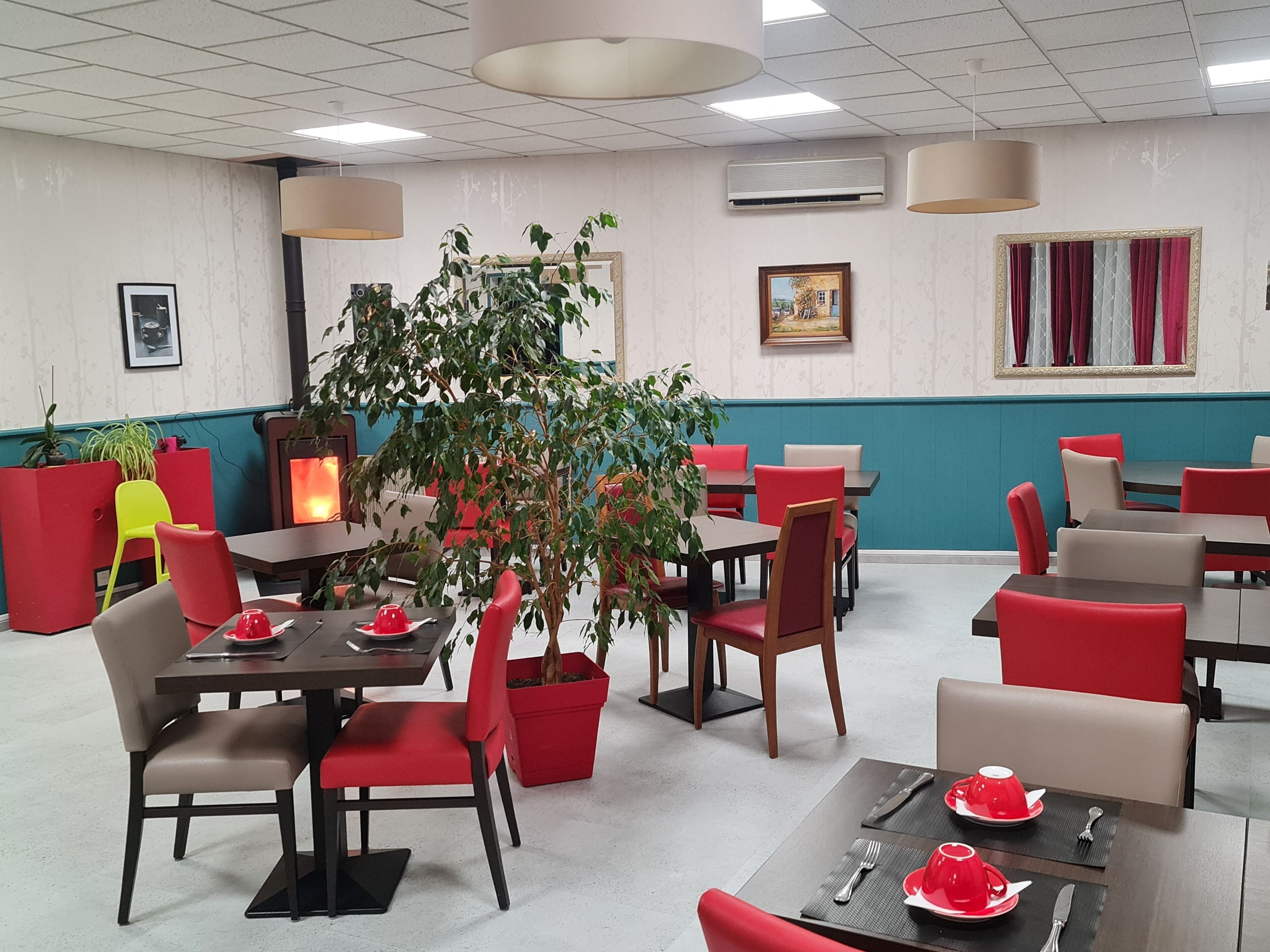 A restaurant with tables and chairs, a large potted plant, and framed pictures on the walls.
